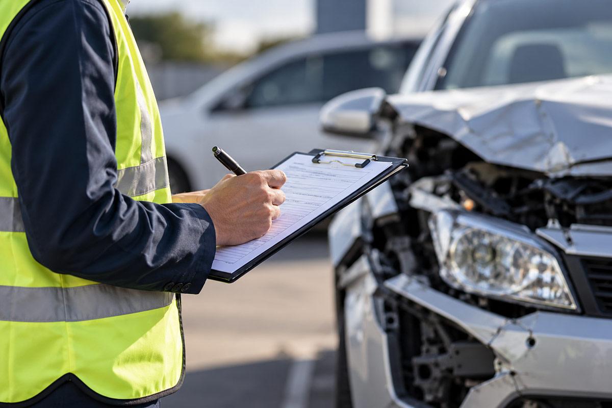 Accident reconstruction expert inspecting vehicle damage and documenting evidence following a road traffic collision.